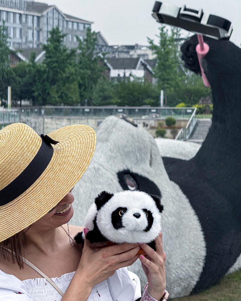 Primer plano de Marta mostrando un panda de peluche con el Selfie Panda de Dujiangyan al fondo, China