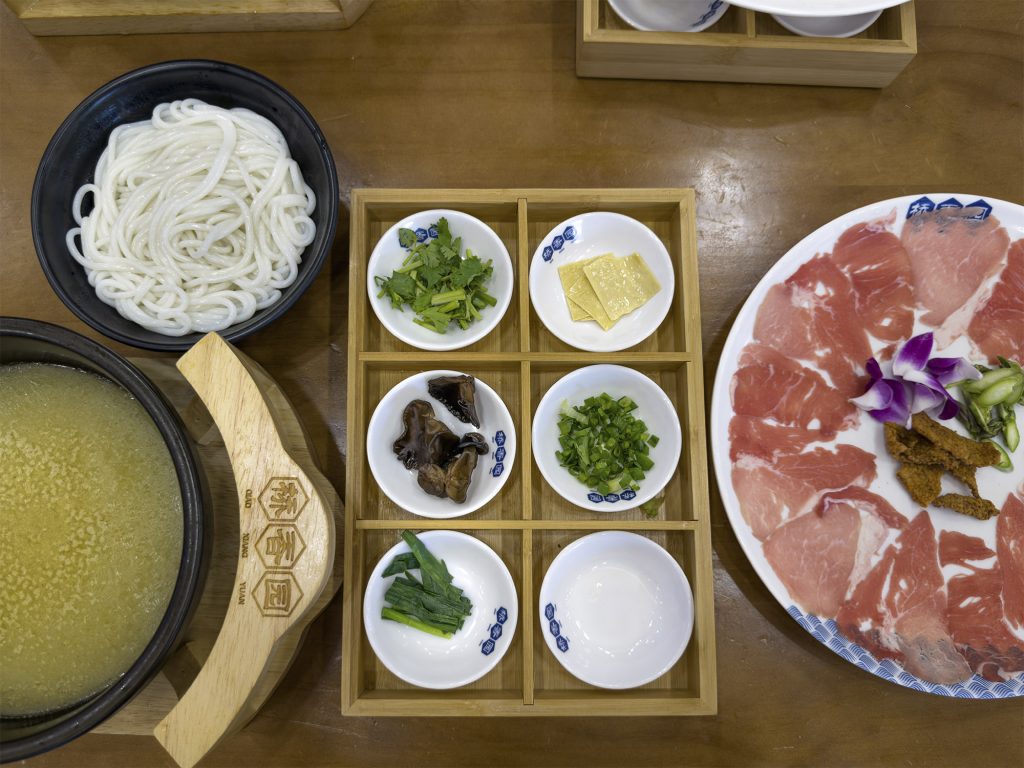 Plato de fideos crossing-the-bridge con caldo humeante e ingredientes crudos, plato emblemático de la gastronomía de Yunnan.