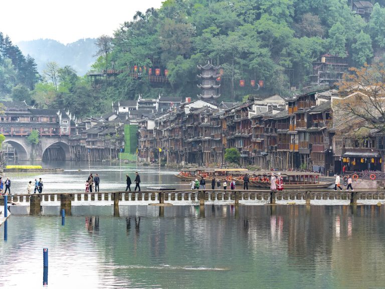 Puente de Madera (Muqiao) de tablones cruzando el río Tuojiang en Fenghuang. El puente más antiguo del pueblo, con orígenes en la dinastía Tang, es una estructura sencilla de tablones de madera que conecta las dos orillas junto al famoso Puente Salto de Roca