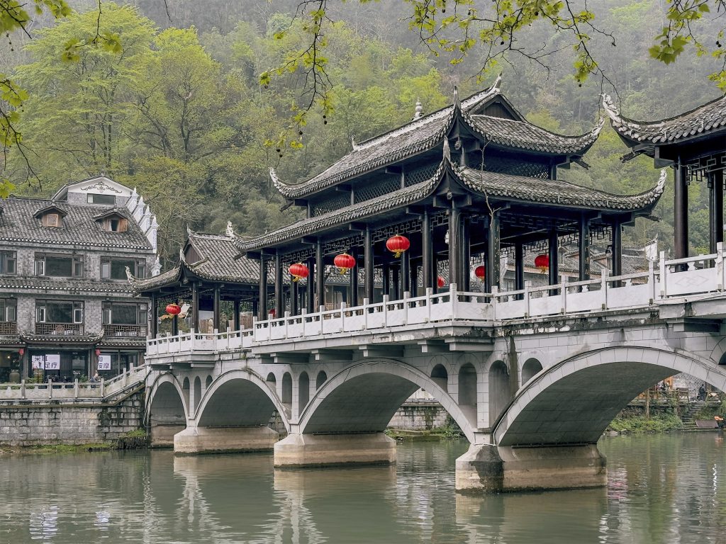 Puente de la Niebla (Wuqiao) de cinco arcos con tres pabellones de estilo oriental en la parte superior, cruzando el río Tuojiang en Fenghuang. El imponente puente paisajístico diseñado por el artista Huang Yongyu se encuentra alejado del centro turístico