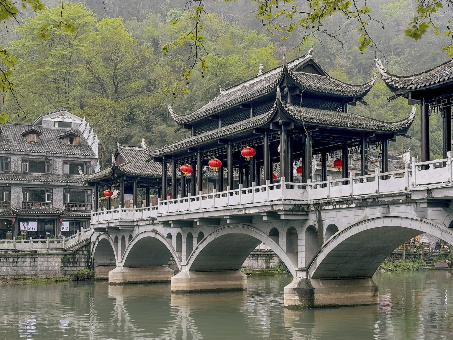 Puente de la Niebla (Wuqiao) de cinco arcos con tres pabellones de estilo oriental en la parte superior, cruzando el río Tuojiang en Fenghuang. El imponente puente paisajístico diseñado por el artista Huang Yongyu se encuentra alejado del centro turístico