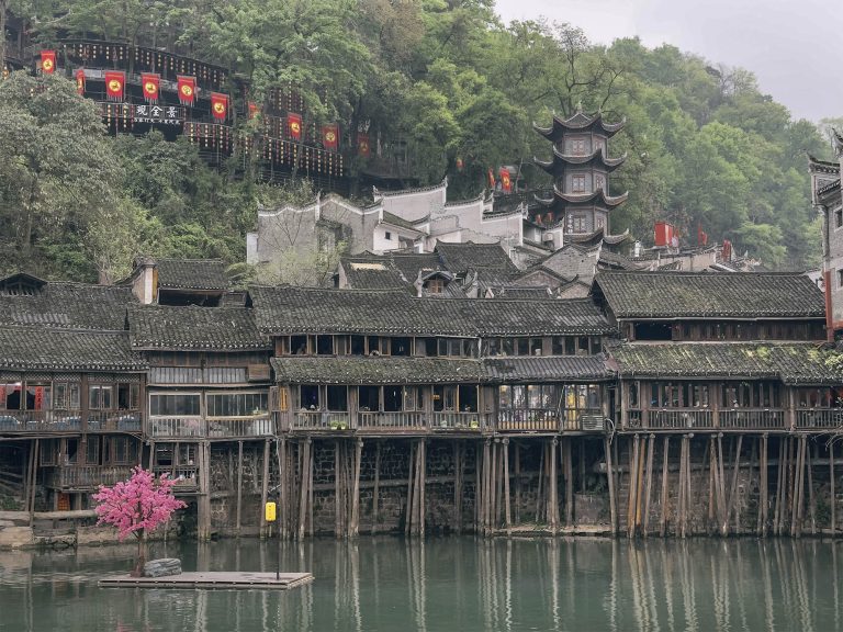 Casas de madera sobre pilotes (Diaojiaolou) construidas sobre el río Tuojiang en Fenghuang. Las típicas viviendas de las etnias Tujia y Miao se elevan sobre pilares de madera directamente desde el agua, con tejados de tejas negras superpuestos y farolillos rojos colgando de los aleros