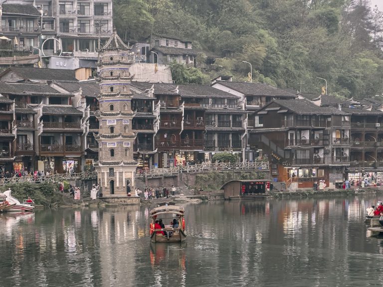 Panorámica aérea de Fenghuang (pueblo del Fénix) con el río Tuojiang serpenteando entre casas colgantes de madera (Diaojiaolou), puentes históricos y montañas neblinosas al fondo, Hunan, China