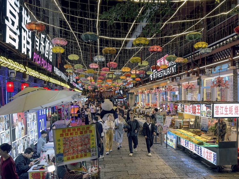 Marta y Javi, de Con un par de maletas, disfrutando de un mercado de comida callejera en China. Puestos con alimentos, ambiente local y luces de colores a su alrededor.
