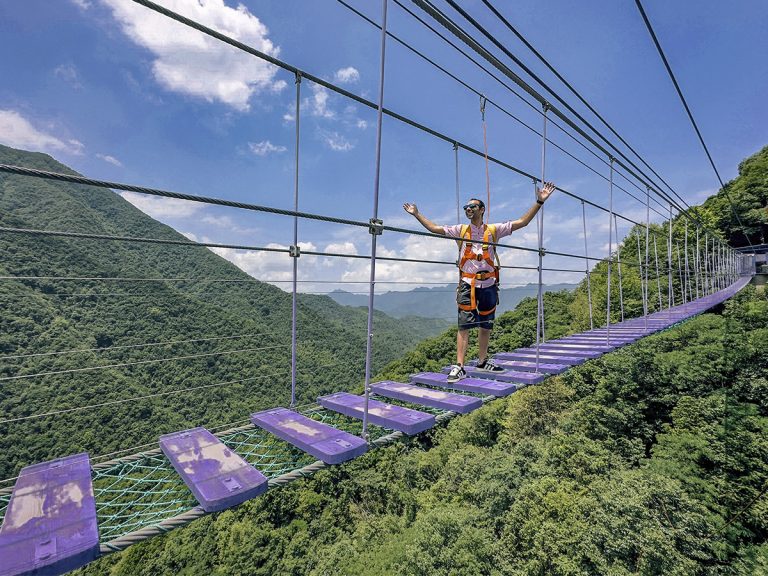 Javi caminando por un puente colgante de tablas con arnés de seguridad en un parque de aventuras en China. Viajar a China es pura aventura.