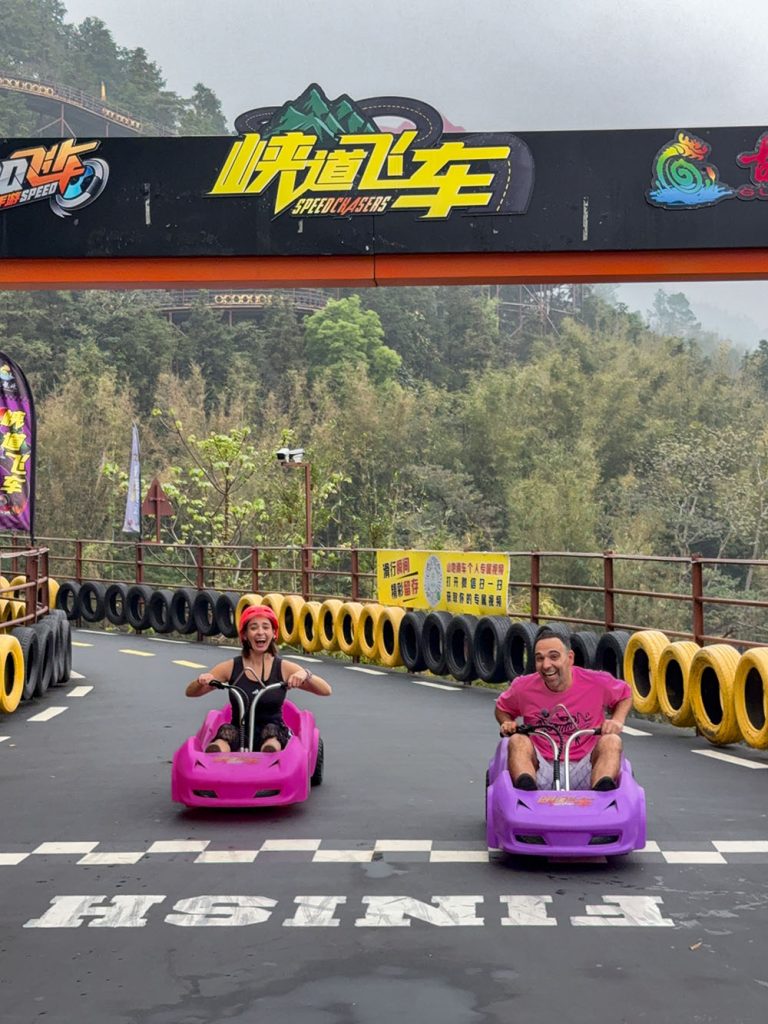 Marta y Javi descendiendo por el circuito de Gulongxia en Guangdong, China, montados en dos coches de carreras estilo Mario Kart. El trazado serpentea entre montañas y bosques con curvas cerradas y vistas espectaculares. Una de las experiencias más divertidas en los parques de aventura de China.