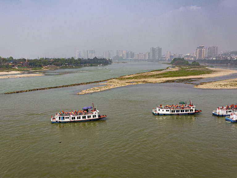 Vista panorámica desde el mirador de la cabeza del Gran Buda de Leshan, con el río serpenteando entre montañas verdes, barcos navegando y el paisaje natural bajo un cielo azul despejado.