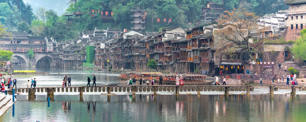 Vista panorámica desde lo alto del Puente de Nieve (雪桥 - Xuě Qiáo) en la ciudad antigua de Fenghuang, China. Se aprecian los tejados tradicionales de la ciudad, el río Tuo serpenteando entre edificios antiguos y las montañas al fondo. Representa una de las mejores perspectivas de la ciudad desde este emblemático puente mirador de dos plantas.