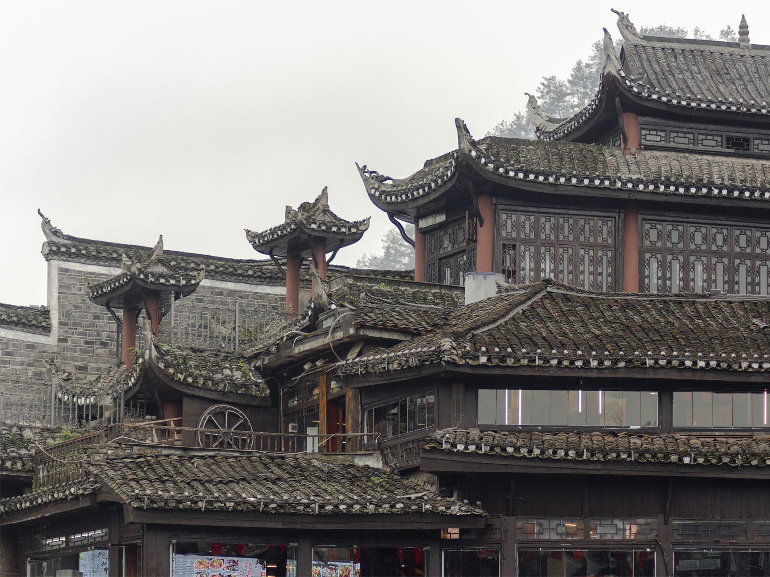 Vista de los tejados tradicionales de tejas negras (yin-yang tiles) de Fenghuang con aleros curvos y voladizos (flying eaves) sobre el río Tuojiang. Las típicas cubiertas inclinadas y las tejas superpuestas de los edificios históricos de la dinastía Ming y Qing en el casco antiguo de Fenghuang, Hunan