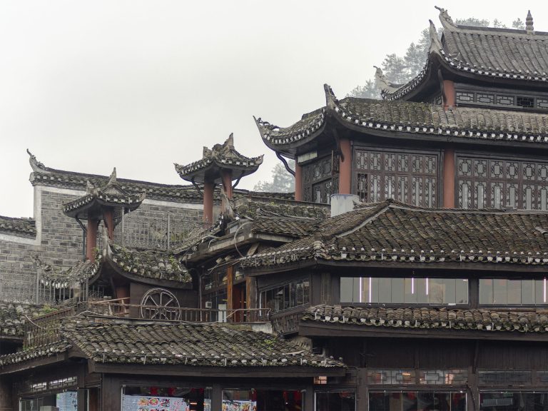 Vista de los tejados tradicionales de tejas negras (yin-yang tiles) de Fenghuang con aleros curvos y voladizos (flying eaves) sobre el río Tuojiang. Las típicas cubiertas inclinadas y las tejas superpuestas de los edificios históricos de la dinastía Ming y Qing en el casco antiguo de Fenghuang, Hunan