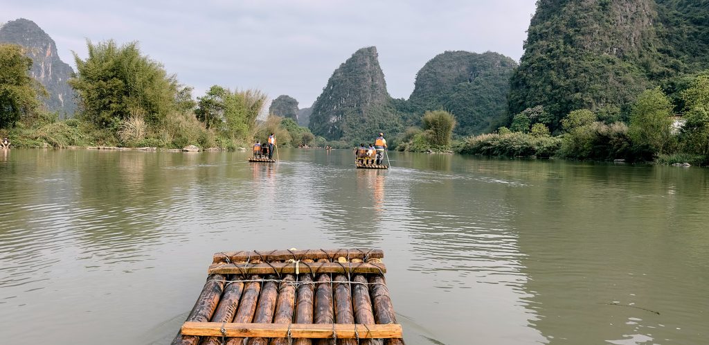 Barca de bambú tradicional navegando por el río Li en Yangshuo, con montañas kársticas de fondo y un barquero remando de pie, como imagen de portada del artículo sobre salud y seguro de viaje en China.