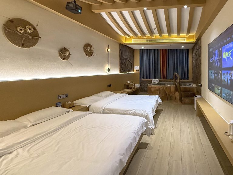 Habitación estilo cueva en el Pinmeiju Hot Spring Cinema Hotel de Dujiangyan, con cama king size, iluminación tenue, diseño de paredes rocosas y una gran bañera de hidromasaje privada en la zona de la habitación.