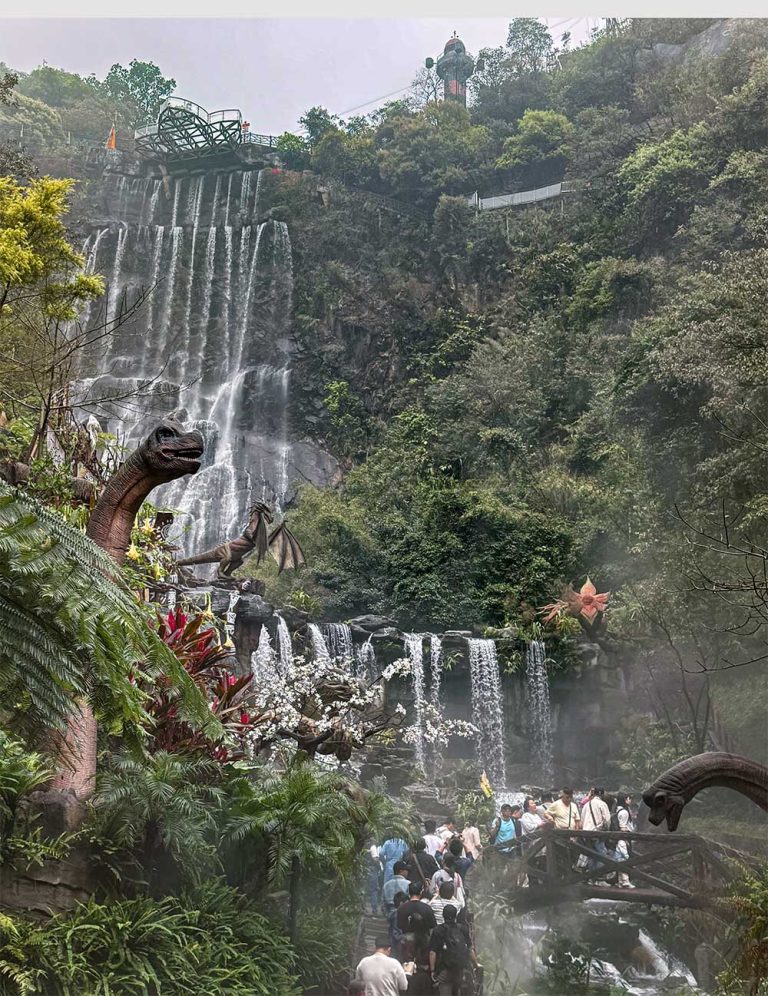 Vista lateral de la cascada principal de Gulong Gorge con dinosaurios animatrónicos entre la vegetación, Qingyuan, China