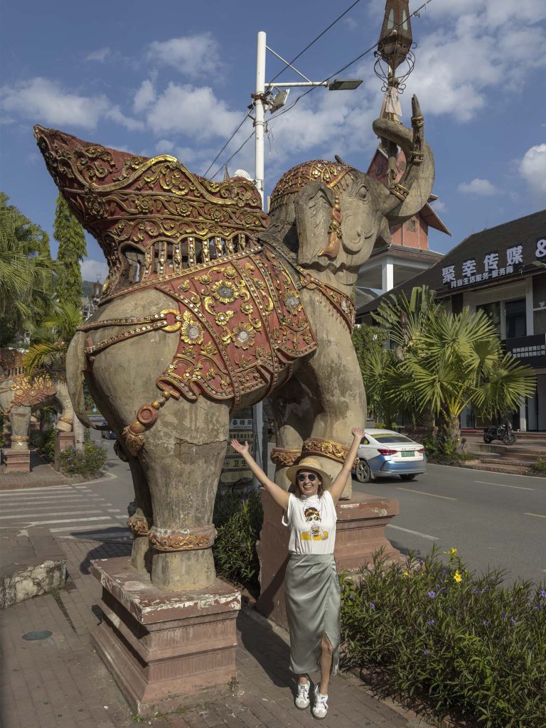 Marta caminando bajo una gran escultura de elefante en una calle de Jinghong, Xishuangbanna, China