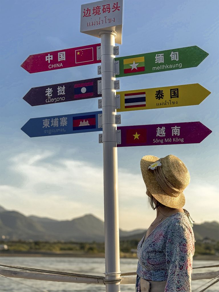 Marta leyendo una señal con las distancias a Tailandia, Laos y Myanmar en el Triángulo Dorado, Xishuangbanna, China