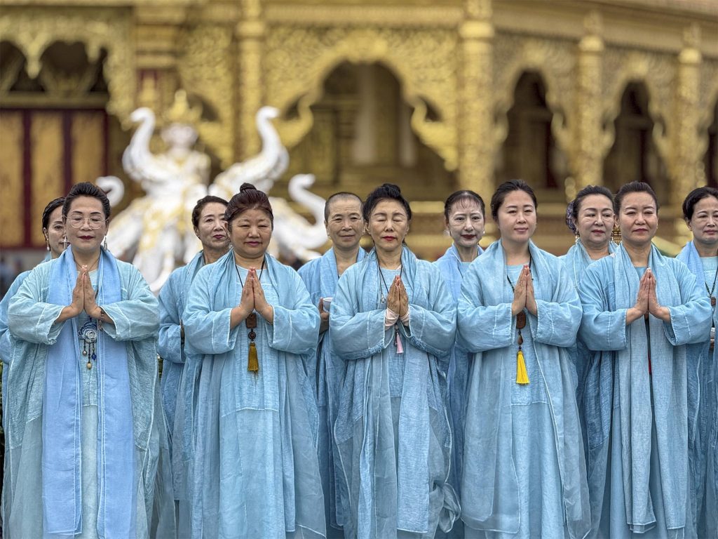 Monjas budistas con túnicas azules rezando y cantando en el interior del Templo del Gran Buda de Mengle, Xishuangbanna, China