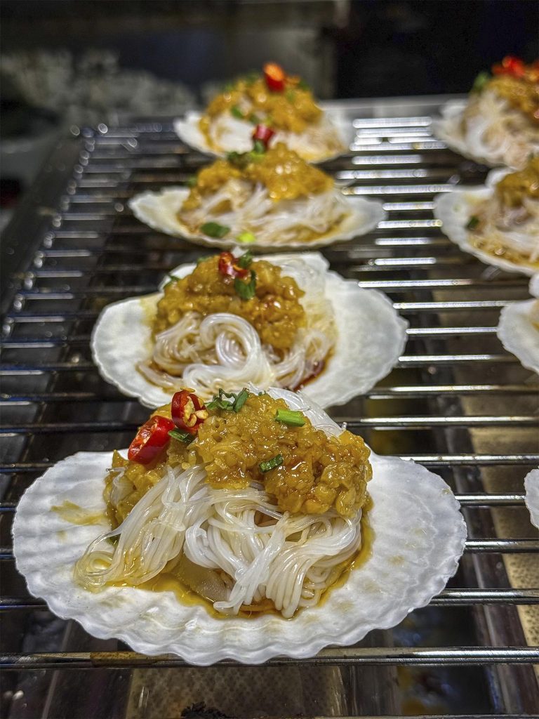 Vieiras a la parrilla cocinándose en un puesto del mercado nocturno de Jinghong, Xishuangbanna, China
