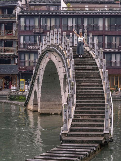 Puente de la Luna (Yueqiao) en Fenghuang, con su característico tramo central altamente arqueado y pasarelas de piedra exteriores que hay que saltar. El puente cruza el río Tuojiang en la zona más tranquila del pueblo del Fénix, lejos del centro turístico
