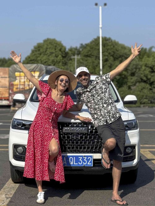 Dos personas posando delante de un SUV blanco con matrícula china durante un viaje por China