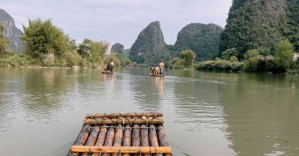 Barca de bambú tradicional navegando por el río Li en Yangshuo, con montañas kársticas de fondo y un barquero remando de pie, como imagen de portada del artículo sobre salud y seguro de viaje en China.