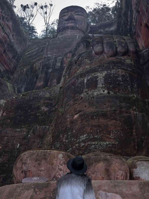 Marta de pie junto al dedo gordo del pie derecho del Gran Buda de Leshan, mostrando la enorme escala de la estatua de 71 metros con la cabeza elevada hacia la cima