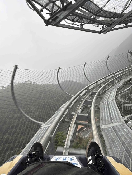Marta y Javi descendiendo en un trineo monoplaza sobre raíles por el circuito de montaña de Gulongxia en Qingyuan, Guangdong, China. El trazado tiene 3,68 kilómetros de longitud, 260 metros de desnivel y 28 curvas, incluyendo varias en horquilla. Una experiencia de velocidad y adrenalina entre bosques y montañas.