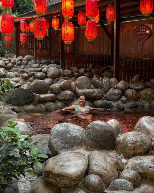 Vista de las piscinas termales al aire libre de Lingxiu en el Monte Emei, con el vapor flotando sobre el agua, rodeadas de vegetación y árboles centenarios, con las montañas de Sichuan al fondo.